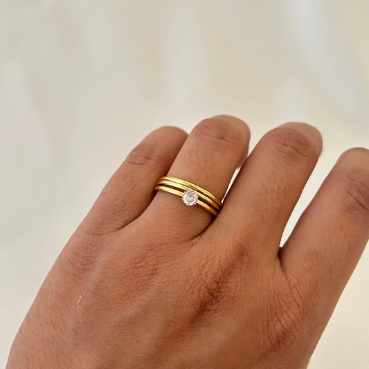 Hand wearing a gold triple-band ring with a small round stone set in the center.