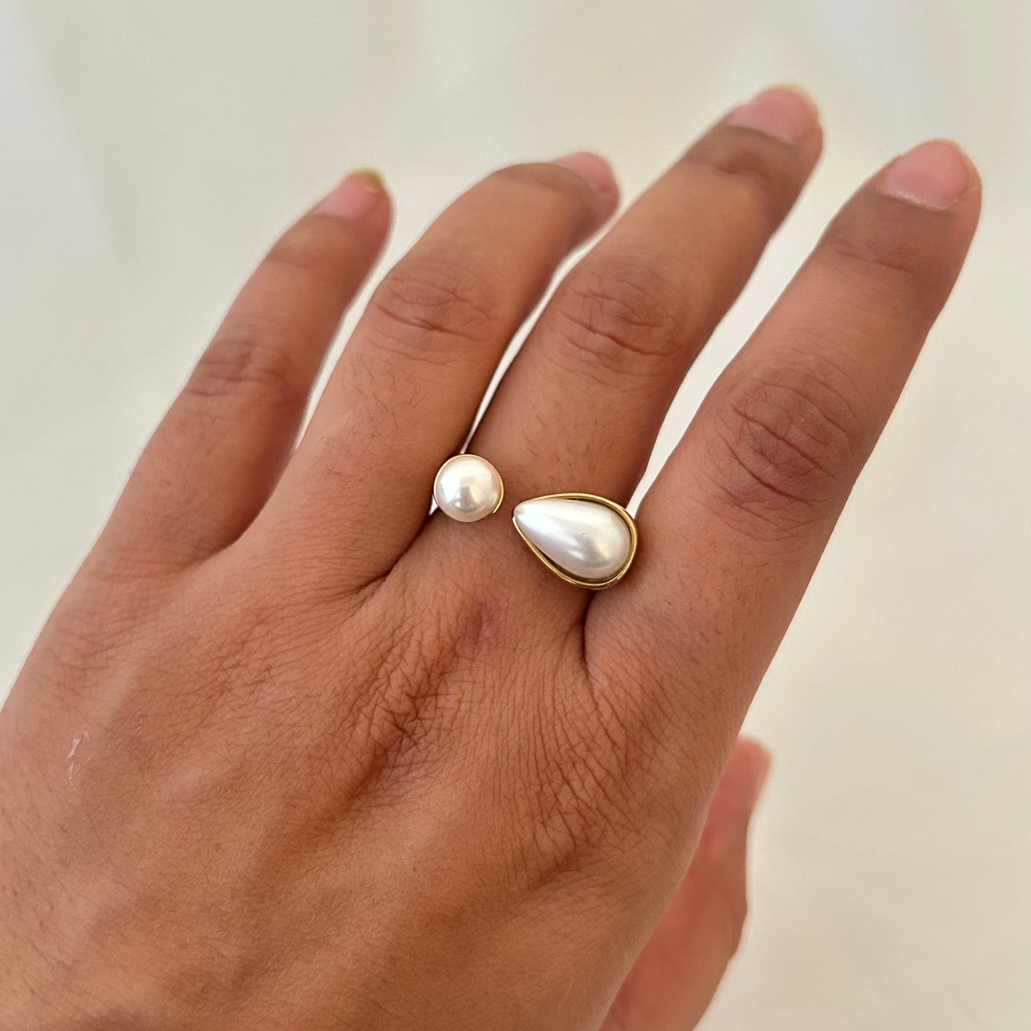 Hand wearing a gold open ring with one round pearl and one teardrop-shaped pearl.