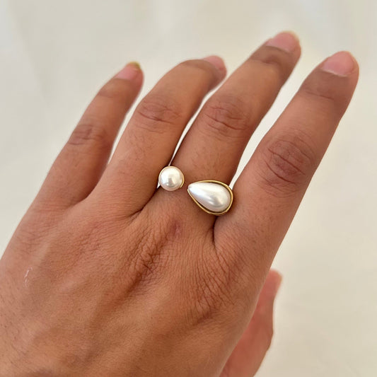 Hand wearing a gold open ring with one round pearl and one teardrop-shaped pearl.
