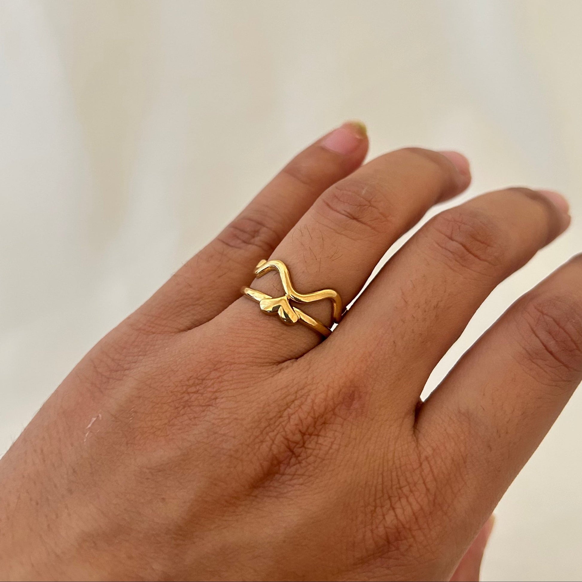 Hand wearing a gold abstract snake-shaped ring with an open, flowing design.