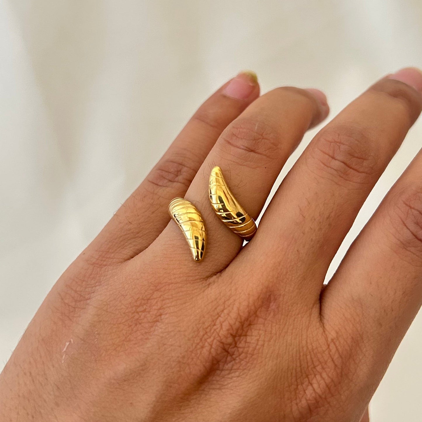 Hand wearing a gold ring with two curved claw-like ends wrapping around the finger.