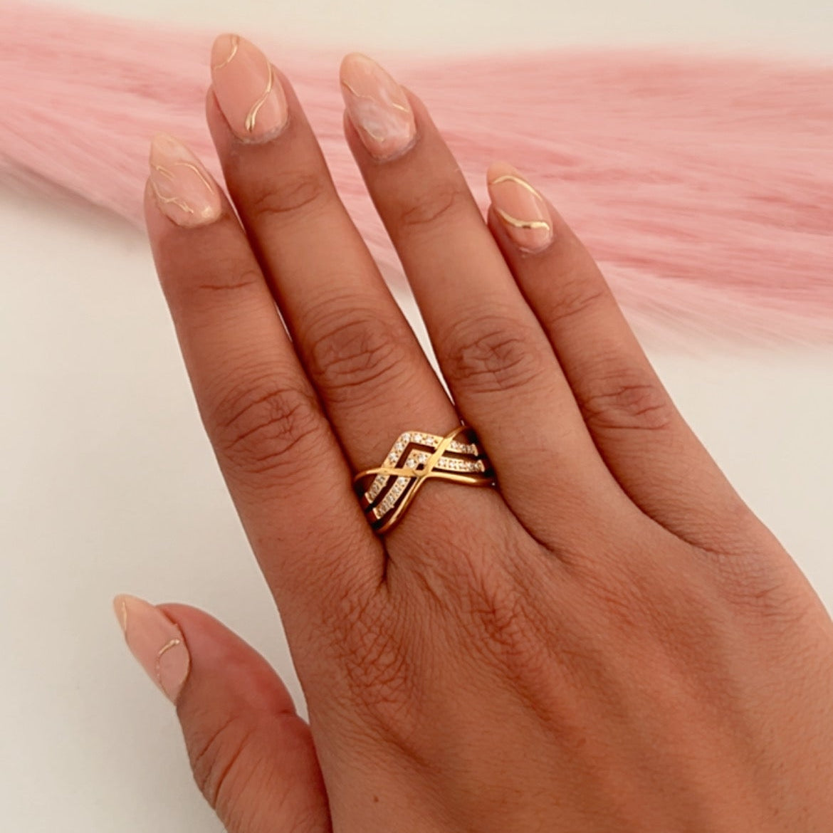 Hand wearing a gold crossover ring with intertwined bands and subtle crystal accents.