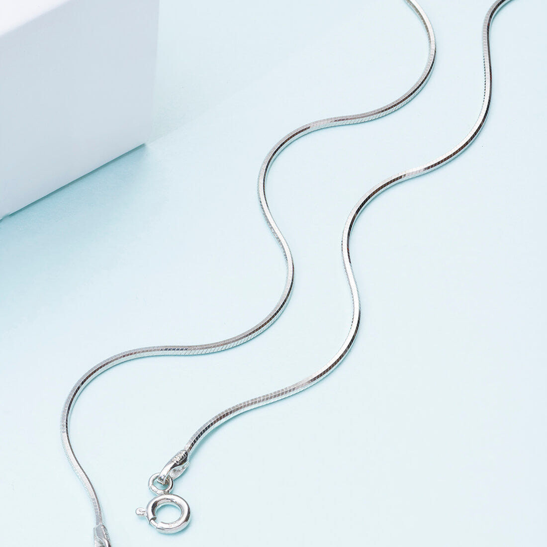 Sleek 925 Sterling Silver snake chain anklet for women on a light blue surface. Minimalist everyday jewellery – Zavya