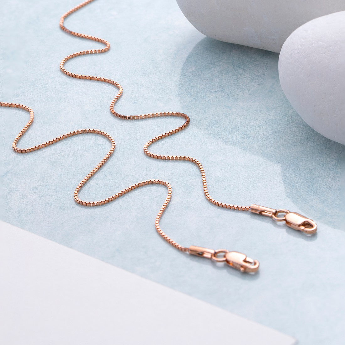 Rose gold 925 Sterling Silver box chain anklet for women placed in waves near white pebbles – Zavya