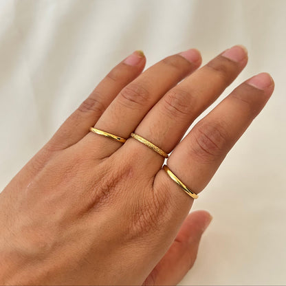Hand wearing two stacked gold rings with fine textured detailing.