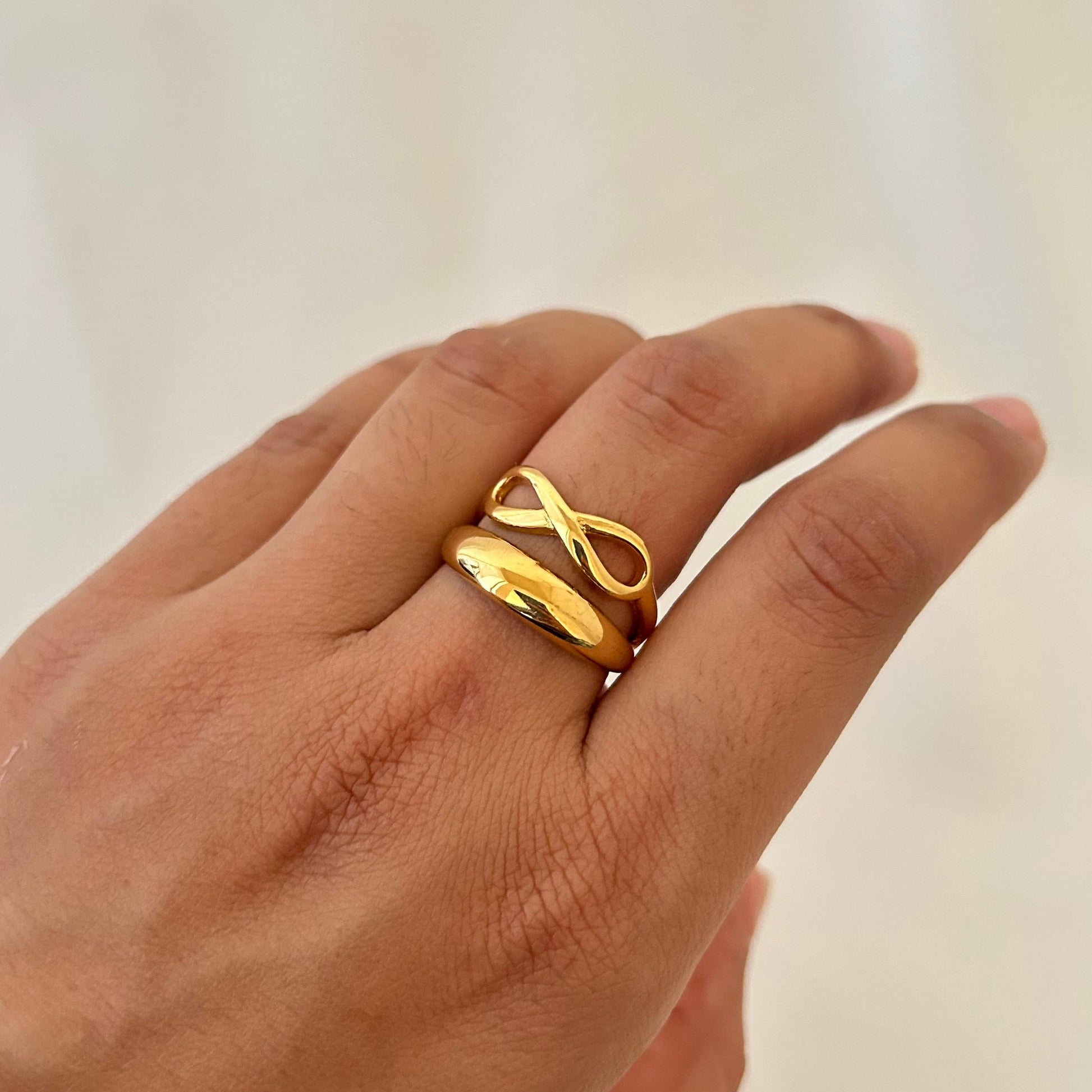 Hand wearing a thick gold ring with an infinity knot design on top.