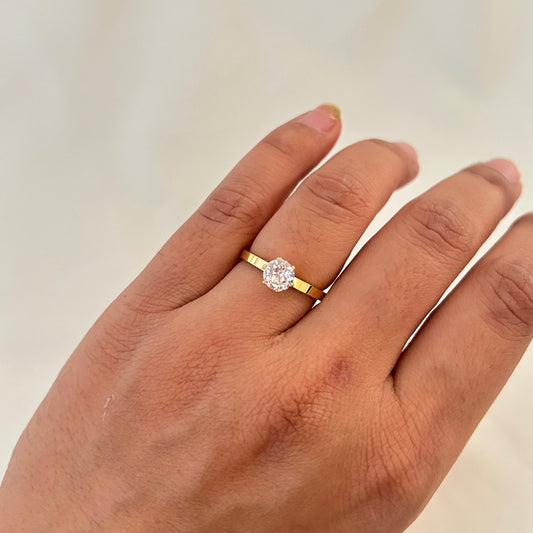 Hand wearing a gold ring with a single oval-cut clear gemstone on a thin polished band.