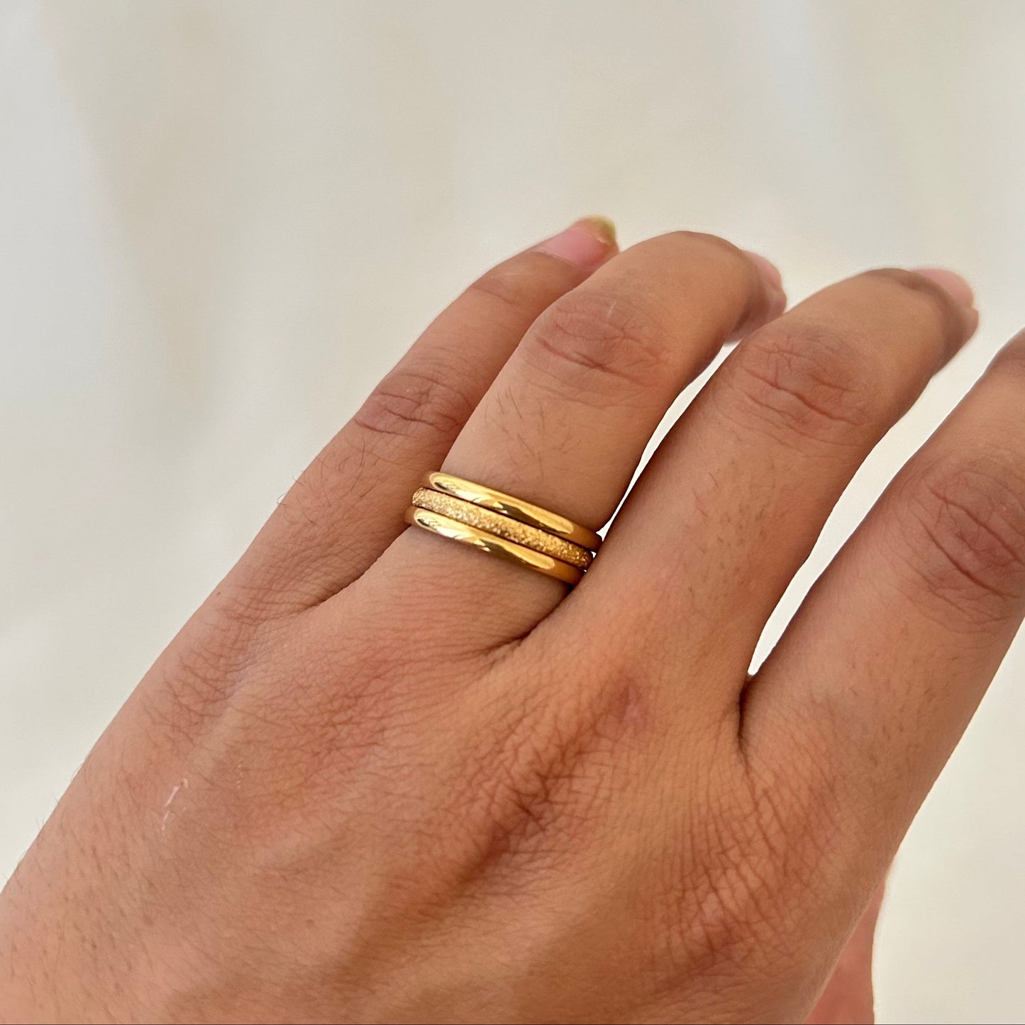 Hand wearing two stacked gold rings with fine textured detailing.